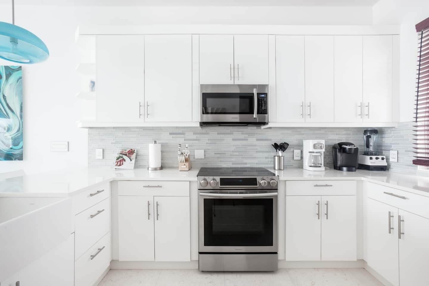 A modern kitchen with white cabinets, a stainless steel oven, a microwave, and a coffee maker.