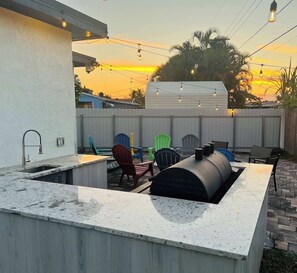 Un área de cocina al aire libre con una parrilla empotrada, asientos exteriores con sillas y vistas al atardecer.