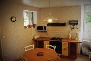 A compact kitchen with a dining table, a microwave, a stove, and a hanging pot rack.