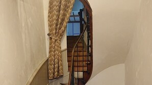 A spiral staircase with a wooden handrail and a chair by the radiator.