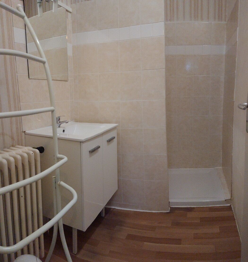 Un baño con lavamanos blanco, un espejo, ducha y un radiador.