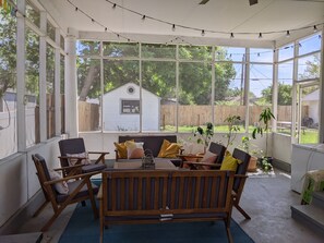 A sunroom with a wooden bench and chairs, large windows, and a view of a backyard.