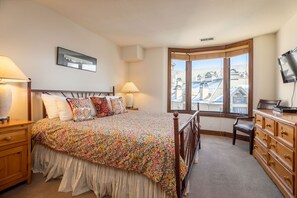 Camera da letto con un letto grande, due comodini, una cassettiera, una televisione e una finestra con vista sugli edifici.