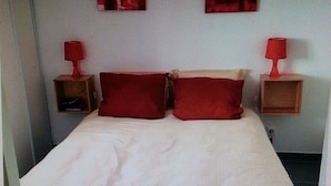 A bed with a striped bedspread, two red pillows, and two bedside tables with red lamps. - T2 recent, air-conditioned, Ideal 50 m from the beach with its private parking space! (Saint-Cyr-sur-Mer)
