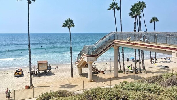 Une plage avec un pont de verre, des palmiers et une tour de surveillance pour les sauveteurs.