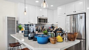 A modern kitchen with white cabinets, a central island with various appliances, and a stainless steel refrigerator.