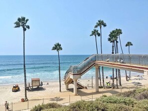 A beach with a glass bridge, palm trees, and a lifeguard tower.