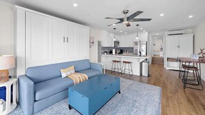 A modern living room with a blue sofa, a coffee table, and a kitchen area with white cabinets and a bar.