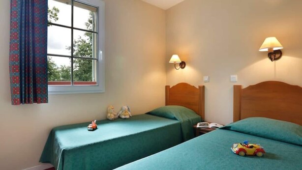 Une chambre avec deux lits, une fenêtre avec des rideaux, une lampe et une voiture jouet sur le sol.