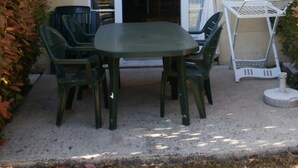Une terrasse extérieure avec une table et des chaises, un étendoir à linge en métal blanc et une porte donnant sur un espace intérieur.