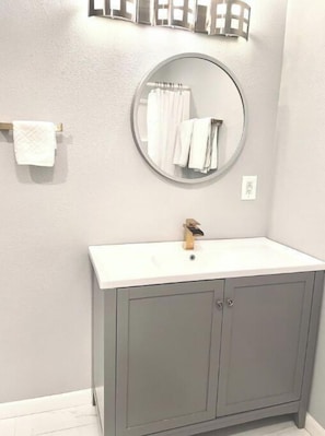 Une salle de bain avec un miroir rond, un lavabo blanc et des meubles gris.