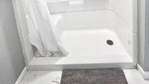 A corner shower with a white curtain, a handheld showerhead, and a small shelf with toiletries.