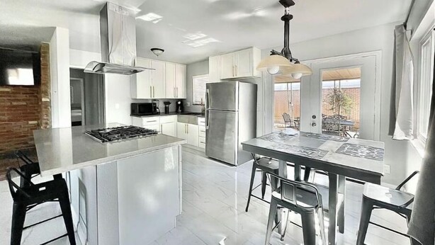 A modern kitchen with white cabinets, a stainless steel refrigerator, and a central island with bar stools.