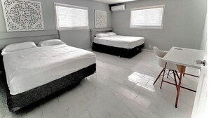 A modern bedroom with two beds, a ceiling fan, and a small desk area.