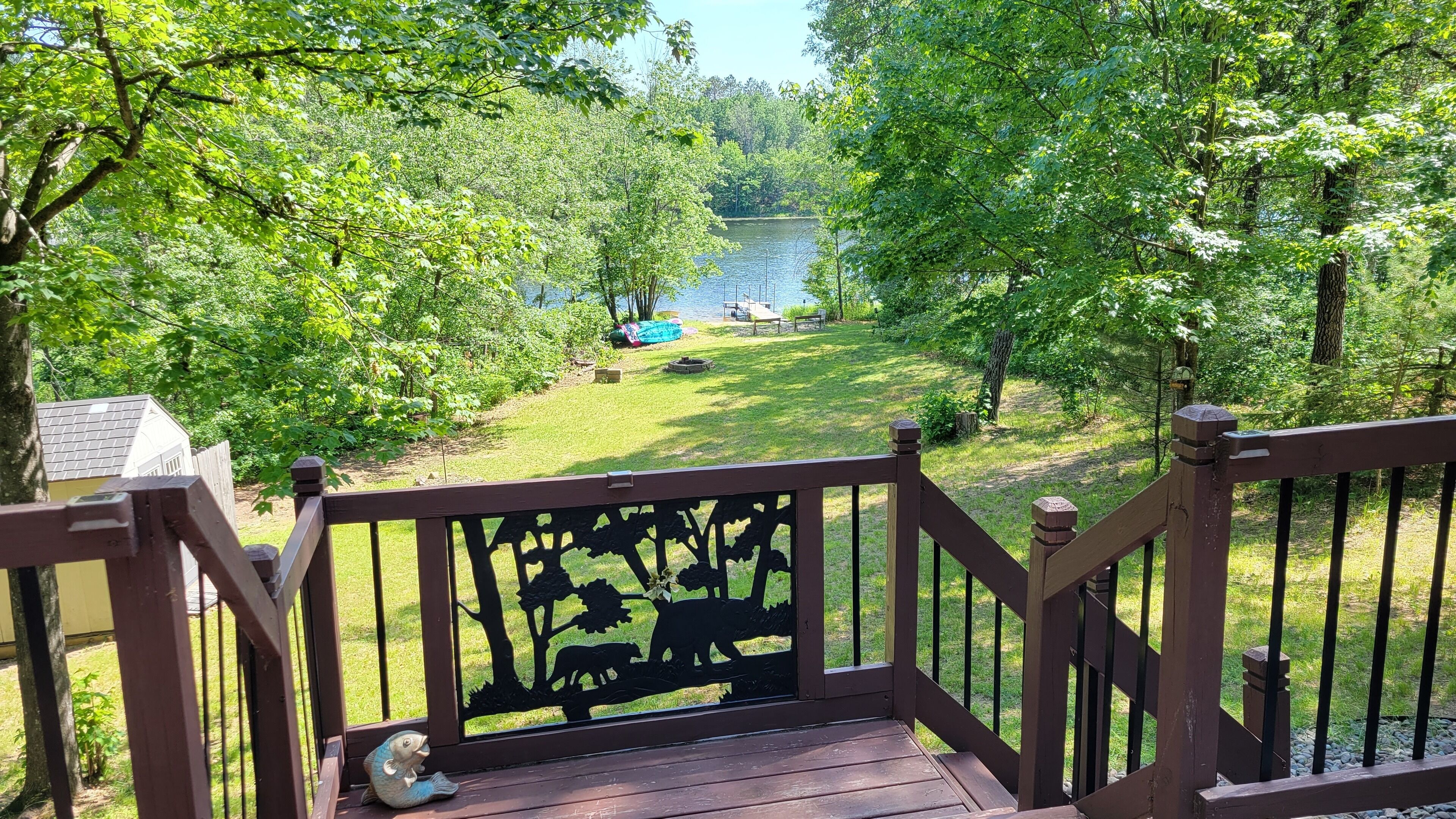 A wooden deck with a railing overlooking a grassy area with trees and a lake.