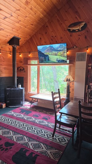 A cozy cabin interior with a wooden interior, a large TV screen, a fireplace, and a view of the outdoors.
