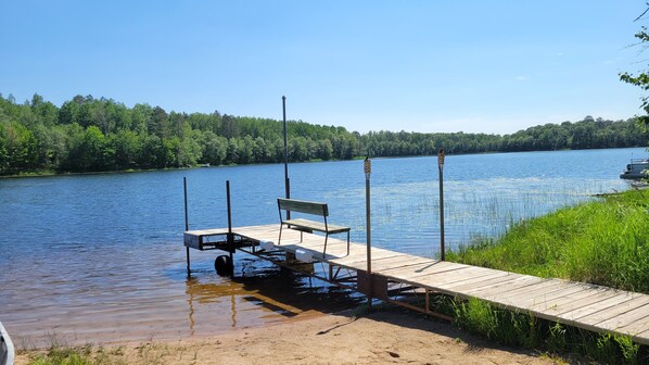 A wooden dock extending into a lake with a bench and a small boat.