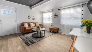 A modern living room with a brown leather sofa, a round coffee table, and a white dining table with yellow flowers. - MODERN/Mins to Beach/walk to dwtn/Free parking (Tarpon Springs)