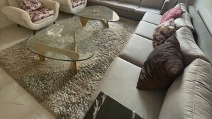 Una sala de estar moderna con un sofá, dos sillones, una mesa de centro de vidrio y una lámpara colgante decorativa.