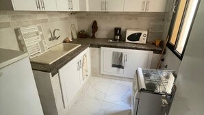 Una cocina compacta con armarios blancos, un microondas, una estufa a gas y un lavamanos.