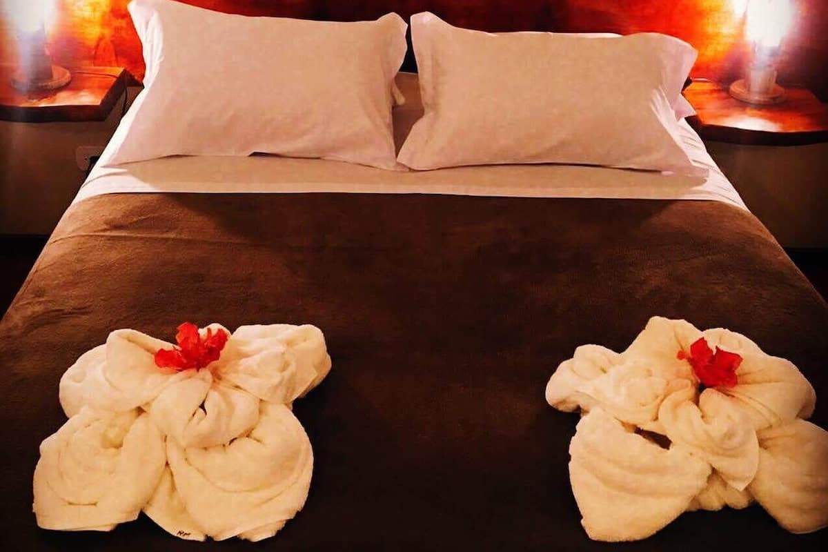 Quarto de hotel com cama, duas almofadas e duas toalhas com flores vermelhas.