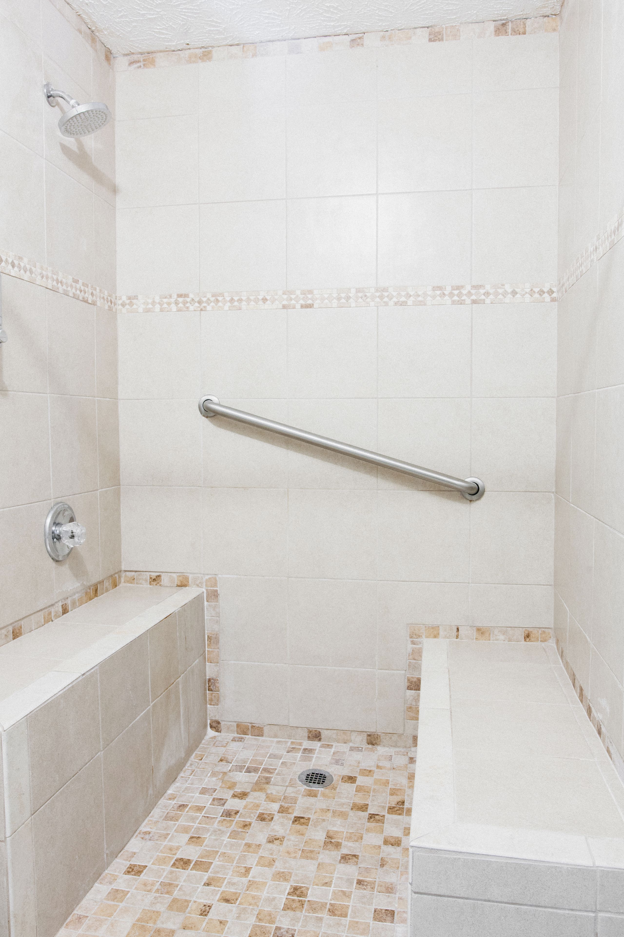 Un espace douche équipé d’une barre d’appui, d’une baignoire et d’un sol carrelé.