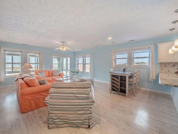 Relax in a spacious living area with a high ceiling, featuring a comfortable sofa set and dining table near a window with an outdoor view.