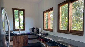 A modern kitchen with wooden cabinets, a stainless steel refrigerator, and a black countertop. There are two windows with wooden frames, and a bar stool is visible. - Casa Aerie – Beach Days, Rooftop Nights (San Francisco)