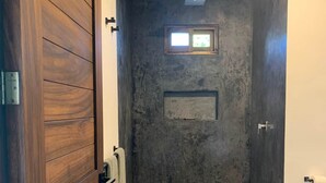 A modern bathroom with a wooden door, a shower area, and a small window. - Casa Aerie – Beach Days, Rooftop Nights (San Francisco)