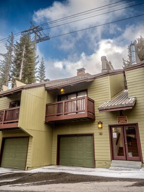A two-story building with a green garage door, a balcony with a brown railing, and a sign warning of danger.