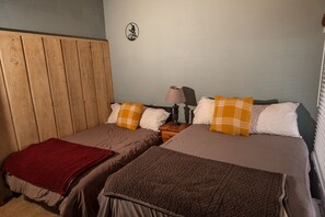 Una habitación con dos camas, cada una con una manta marrón y una manta roja en la cama de la izquierda. Hay una mesita de noche con una lámpara y una pequeña mesa entre las camas.