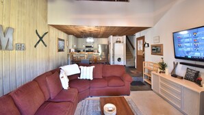 Una sala de estar moderna con un sofá modular, un televisor de pantalla plana y una cocina al fondo.