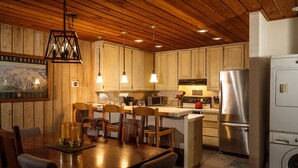 Una cocina moderna con techo de madera, luces colgantes, electrodomésticos de acero inoxidable y una zona de comedor con mesa y sillas.