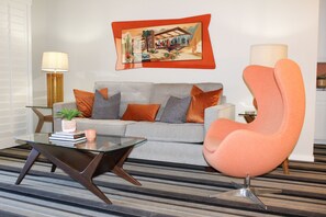 A living room with a sofa, a glass coffee table, a modern armchair, a lamp, and a framed picture on the wall.
