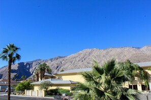 A building with a yellow facade, palm trees in the foreground, and a mountain in the background. - Modern & Chic One Bedroom Condo, centrally located (Palm Springs)