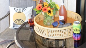 Una mesa redonda de vidrio con una cesta de mimbre que contiene una botella, una lata, gafas de sol y una copa de vino tinto.