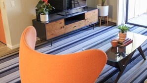 Una sala de estar moderna con un televisor de pantalla plana grande, una mesa de centro de vidrio, un sillón naranja y una alfombra a rayas.