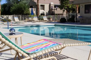 A pool area with lounge chairs and a small table with a decorative item. - Modern & Chic One Bedroom Condo, centrally located (Palm Springs)