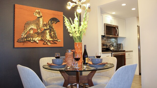 Un comedor con una mesa de vidrio, sillas azules, un jarrón con flores y un cuadro en la pared.
