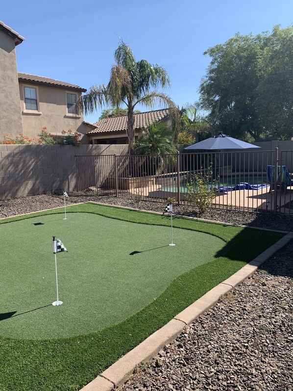 Een midgetgolfbaan met kunstgras, een zwembad en een omheind gebied met een palmboom.