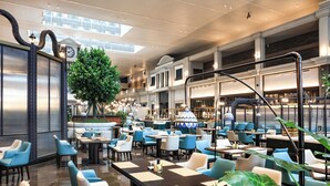 Un vestíbul d'hotel espaiós amb diverses zones de restauració, un gran arbre i un rellotge a la paret.