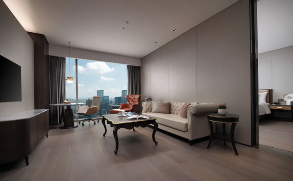 A modern hotel room with a large window offering a city view, a sofa, a coffee table, and a desk area.
