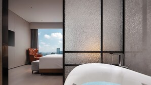 Una habitació d'hotel moderna amb un llit gran, una zona de seients amb una cadira i una banyera.