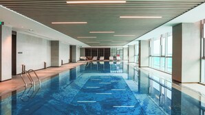 Una piscina interior moderna amb aigua cristal·lina, un paviment de rajoles i un sostre amb il·luminació lineal.
