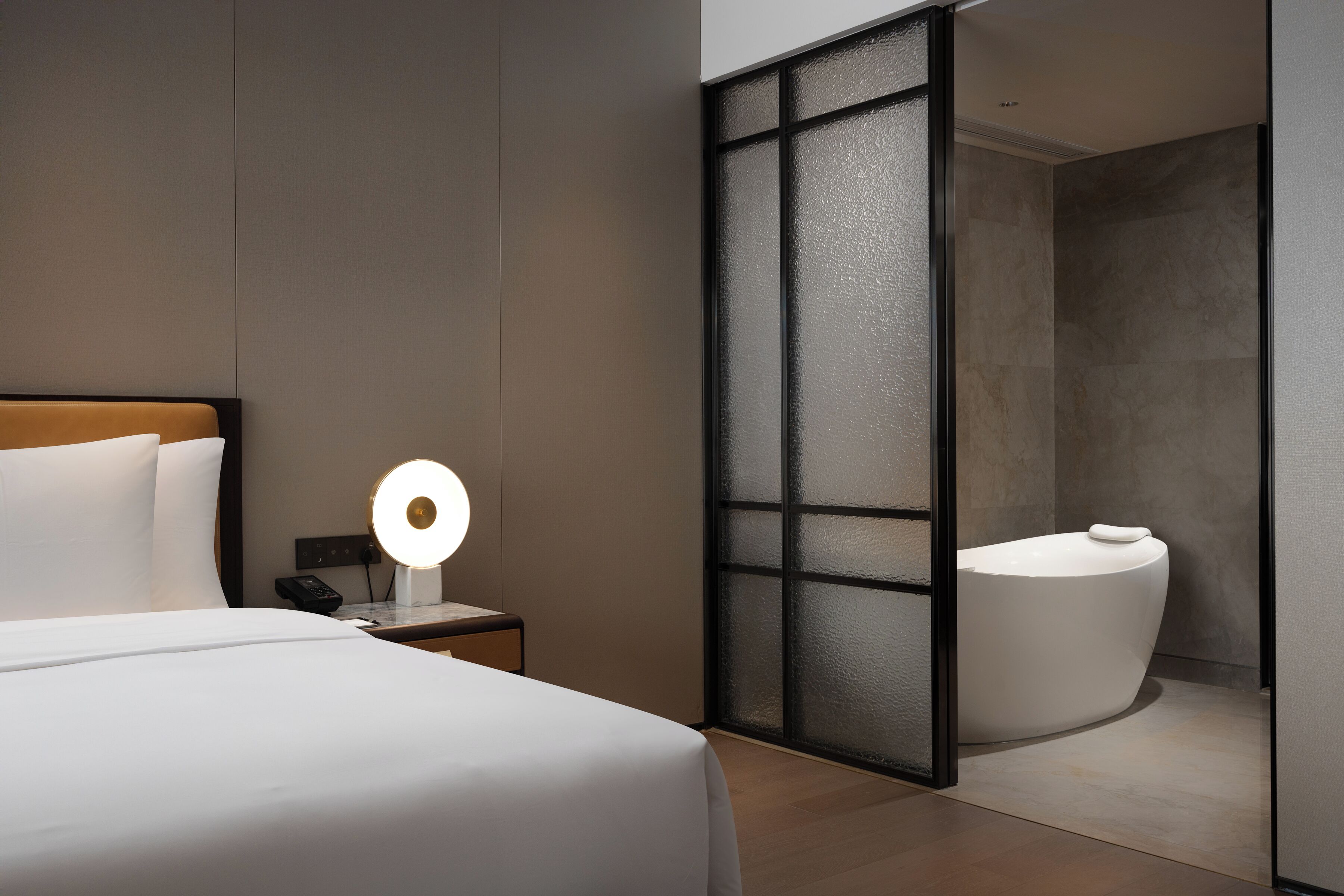 Een moderne hotelkamer met een bed, een bedlampje en een badkamer met een bad.