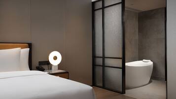 Een moderne hotelkamer met een bed, een bedlampje en een badkamer met een bad.