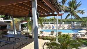 Un espace extérieur abrité comprenant un barbecue, une table de pique-nique et des chaises longues, le tout situé près d’une piscine.