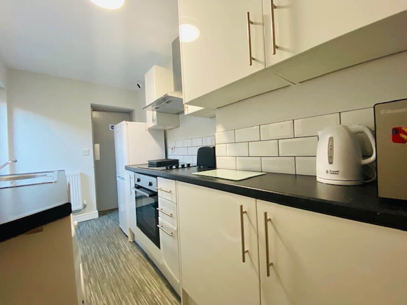 A compact kitchen with white cabinets, a black countertop, and a kettle.