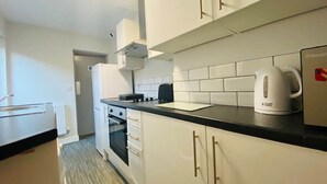 A compact kitchen with white cabinets, a black countertop, and a kettle. - Townhouse @ 110 Etruria Vale Road Stoke (Stoke-on-Trent)