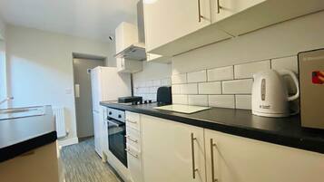 A compact kitchen with white cabinets, a black countertop, and a kettle.